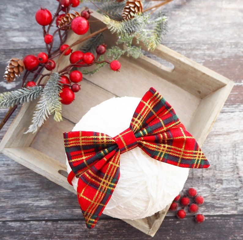 May include: A red and gold plaid bow on a white yarn ball. The bow is tied with a knot in the center and has a frayed edge.
