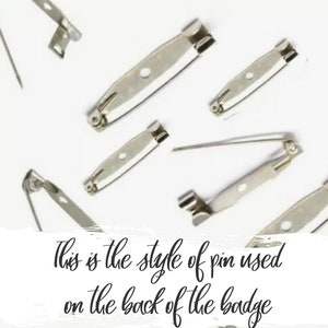 May include: A close-up of several silver-toned safety pin backs. The pins are used to attach badges or other items to clothing.