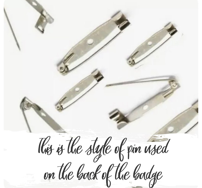 May include: A close-up of several silver-toned safety pin backs. The pins are used to attach badges or other items to clothing.