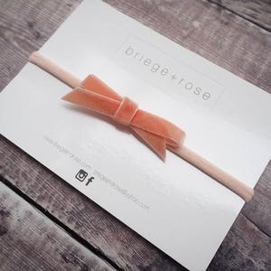 May include: A pale pink velvet bow headband on a white card with the text "briege+rose" and website information.
