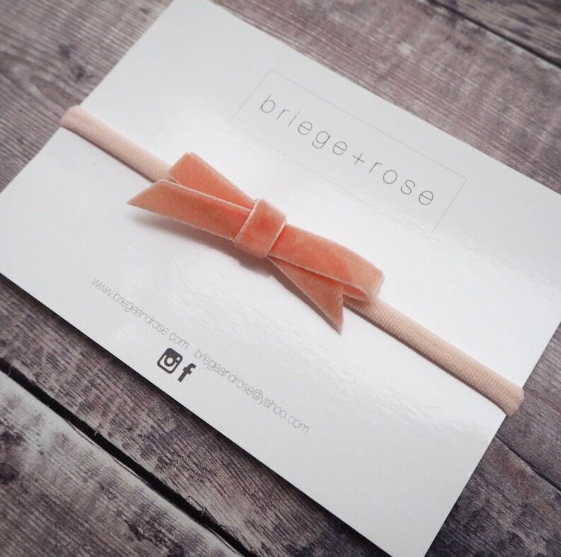 May include: A pale pink velvet bow headband on a white card with the text "briege+rose" and website information.