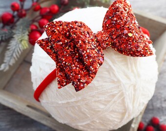 May include: Red glitter bow headband on a white yarn ball.