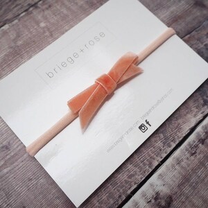 May include: A peach-colored velvet bow headband on a white card with the text "briege+rose" and website information.
