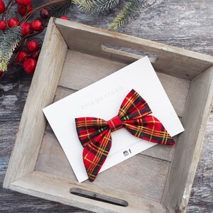 May include: Red and green plaid bow with gold accents. The bow is on a white card with the text "briege+rose" in black.