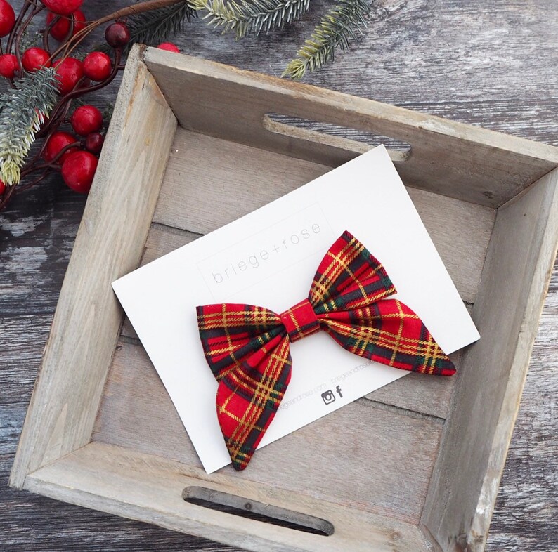 May include: Red and green plaid bow with gold accents. The bow is on a white card with the text "briege+rose" in black.