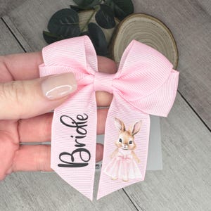 May include: A pink bow with a white bunny illustration and the name "Bridgette" printed on it.