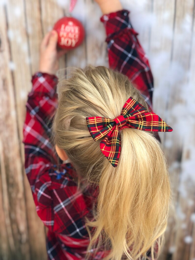 May include: A red and green plaid hair bow with gold accents. The bow is tied in a ponytail.