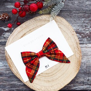 May include: A red and gold plaid bow with a white background. The bow is on a wooden surface with the text "briege+rose" on the white background.