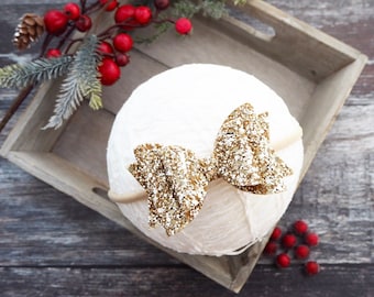 May include: A gold glitter bow headband on a white background. The headband is made of a thin elastic band and the bow is tied in a simple knot.