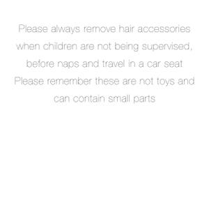 May include: Text on a white background that reads: "Please always remove hair accessories when children are not being supervised, before naps and travel in a car seat. Please remember these are not toys and can contain small parts."