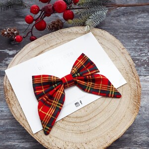 May include: Red and green plaid bow with a white background. The bow is tied in a knot and has a long tail. The text "bridgetrose" is visible in the background.