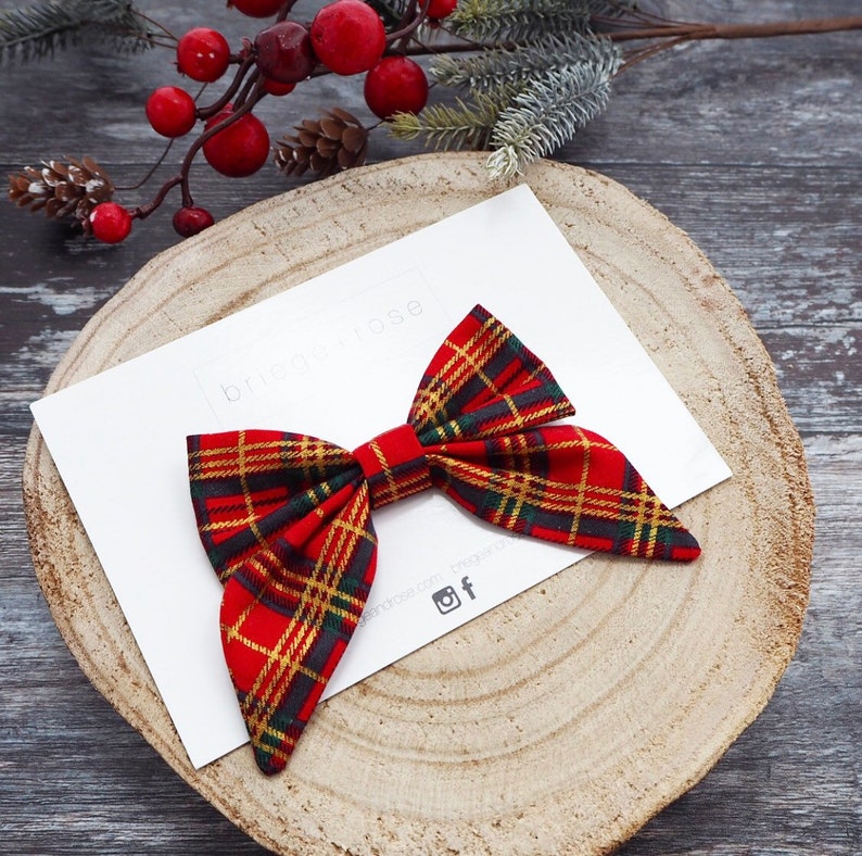 May include: Red and green plaid bow with a white background. The bow is tied in a knot and has a long tail. The text "bridgetrose" is visible in the background.
