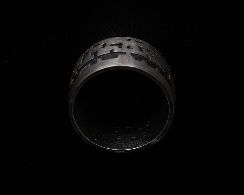 May include: A silver ring with a geometric pattern engraved around the band.