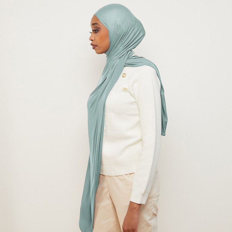 May include: A light blue jersey hijab with a draped style. The hijab is made of a soft, stretchy fabric.