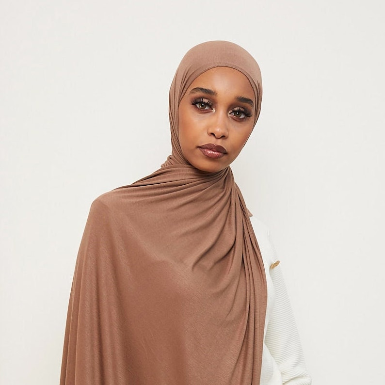 May include: A brown jersey hijab with a simple, elegant drape. The hijab is made of a soft, stretchy fabric and is perfect for everyday wear.