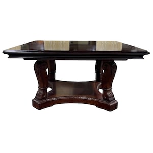 May include: A dark brown wooden dining table with a square top and a carved base. The table has a polished finish and intricate details on the legs.