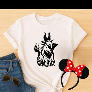 May include: A white t-shirt with a black silhouette of Maleficent from Disney's Sleeping Beauty. The silhouette shows Maleficent with her dragon form and horns, surrounded by flames.