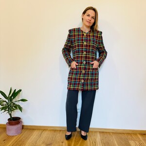 May include: A long-sleeved, multi-colored plaid jacket with gold buttons and pockets. The jacket is worn with dark pants and black shoes. The jacket's colors include red, yellow, blue, and green. The outfit is a vintage style.