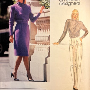 May include: Vogue American Designers sewing pattern featuring two designs by Bill Kaiserman. The pattern number is 2597. The first design is a purple dress with a high neck and long sleeves. The second design is a gray top with a wrap style neckline and white pants.