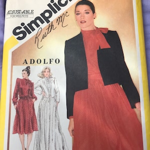 May include: Simplicity sewing pattern for a dress and jacket. The pattern is for size 14, miss petite. The pattern is by Ruth Mc Adolfo. The pattern shows a woman wearing a red dress with a black jacket and a bow tie.