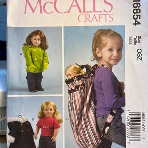 May include: A sewing pattern for a doll carrier, featuring a pink and black striped fabric with floral accents. The pattern is for size OSZ and is from McCall's Crafts.