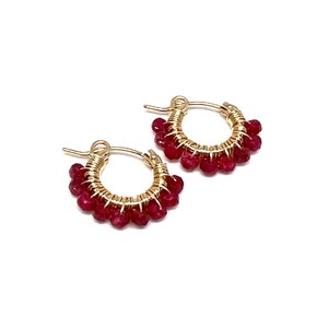 May include: Gold hoop earrings with small red gemstone accents.