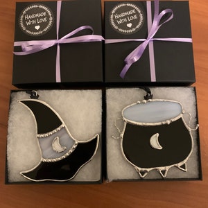 May include: Two black gift boxes with purple ribbon and "Handmade with Love" labels, each containing a stained glass ornament. One ornament is a black witch's hat with a white crescent moon, the other is a black cauldron with a white crescent moon.