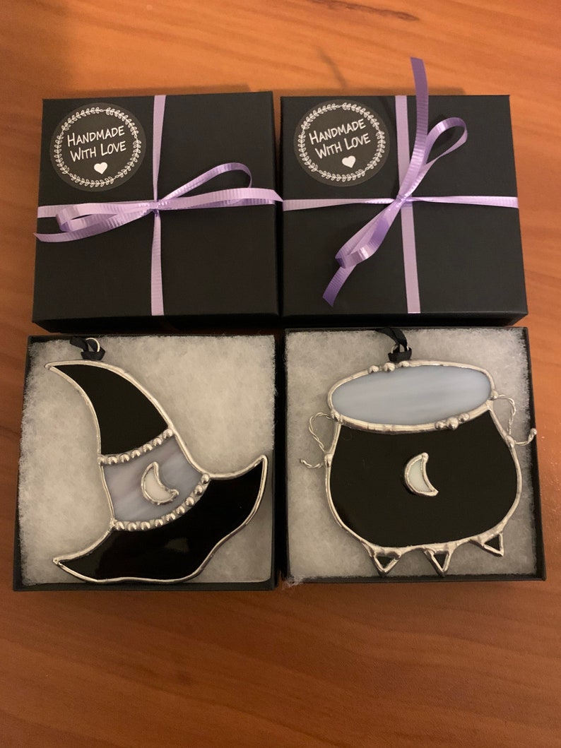 May include: Two black gift boxes with purple ribbon and "Handmade with Love" labels, each containing a stained glass ornament. One ornament is a black witch's hat with a white crescent moon, the other is a black cauldron with a white crescent moon.