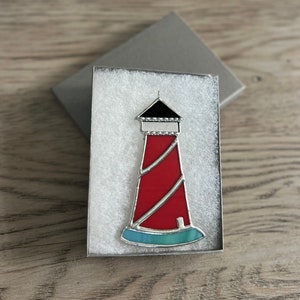May include: A red and white lighthouse with a black roof and a blue base, in a white gift box.