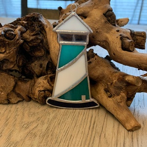 May include: A stained glass ornament shaped like a lighthouse with a white base, a teal body, and a black base.