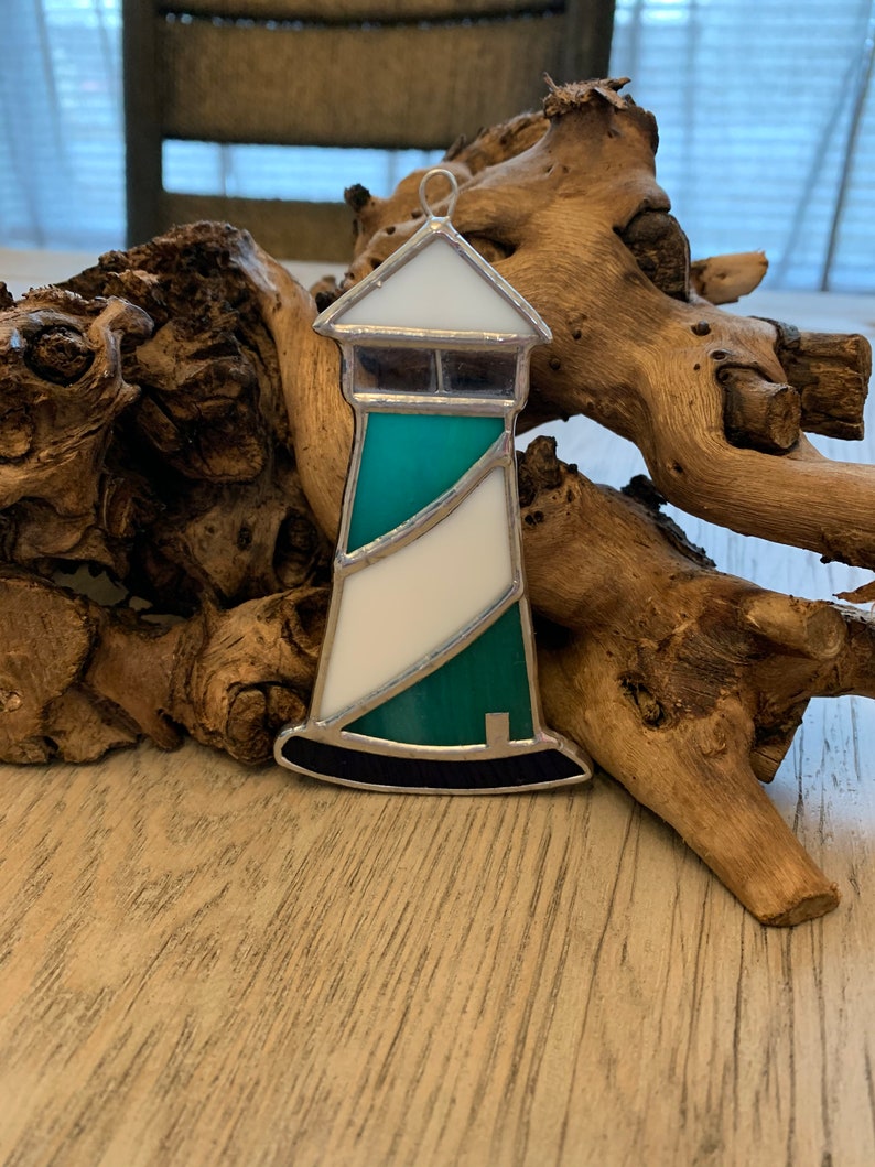 May include: A stained glass ornament shaped like a lighthouse with a white base, a teal body, and a black base.