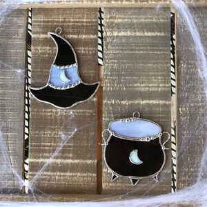 May include: Two stained glass Halloween ornaments, a black witch's hat with a crescent moon and a black cauldron with a crescent moon.