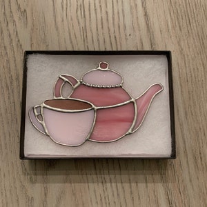 May include: A pink stained glass teapot and cup, with silver accents, in a white box.