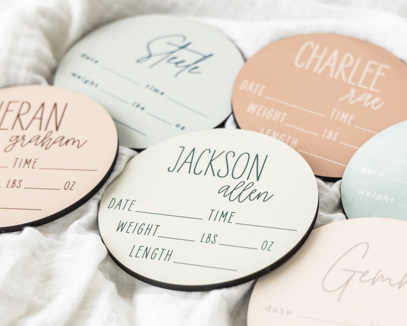 May include: Five round wooden baby announcement plaques with black borders. Each plaque has a different name and the text "Date", "Weight", "Length", "Time", "LBS", and "OZ". The names are "Fran Graham", "Steep", "Jackson Allen", "Charlee Rae", and "Gem".