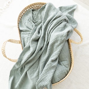 May include: A light blue muslin swaddle blanket in a woven wicker basket.