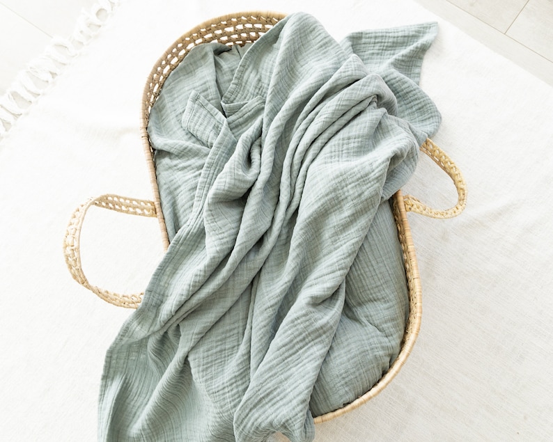 May include: A light blue muslin swaddle blanket in a woven wicker basket.