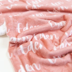 May include: A soft, pink blanket with the name "Eden" repeatedly printed in white script. The blanket is folded, showing the plush texture and a white backing. Ideal for baby gifts.