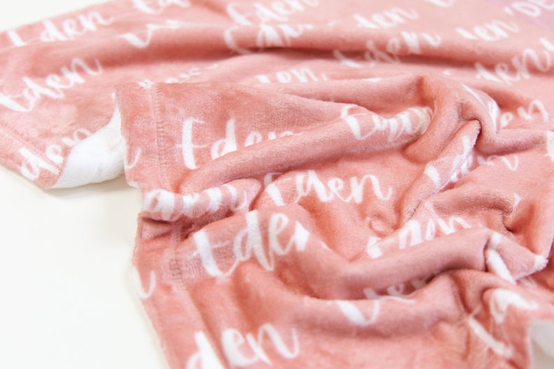 May include: A soft, pink blanket with the name "Eden" repeatedly printed in white script. The blanket is folded, showing the plush texture and a white backing. Ideal for baby gifts.