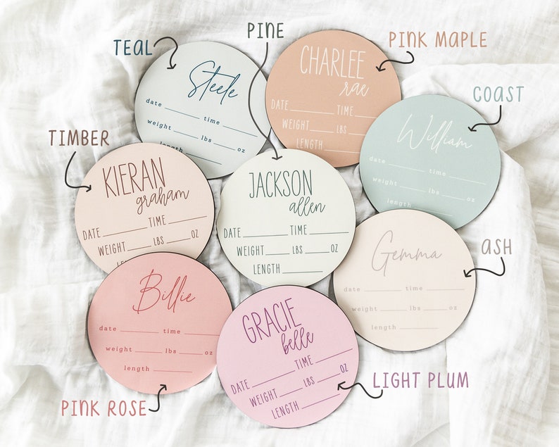 May include: Ten round wooden baby announcement plaques in various colors, including teal, pine, pink maple, coast, ash, light plum, and pink rose. Each plaque has a blank space for a name, date, time, weight, lbs, oz, and length.