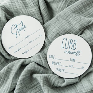 May include: Two white round wooden plaques with black text. The top plaque says "Steele" and has spaces for date, weight in lbs, length in inches, and time in oz. The bottom plaque says "CUBB maxwell" and has spaces for date, weight in lbs, length in inches, and time in oz.