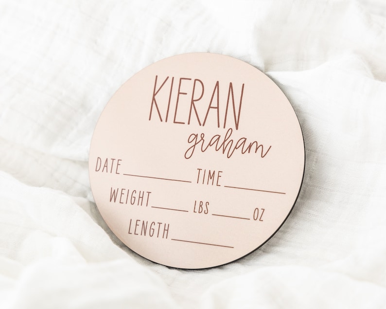 May include: A pink wooden baby announcement plaque with the name "Kieran graham" and spaces to fill in the date, time, weight in pounds and ounces, and length.