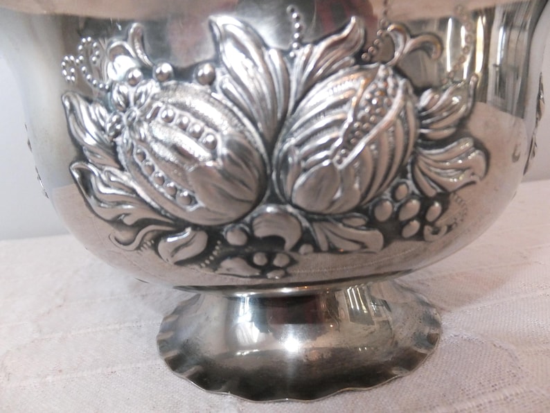 K&ouml;nnte beinhalten: Silberne Schale mit einem verzierten Design aus Blumen und Bl&auml;ttern. Die Schale hat einen gewellten Rand und einen Sockel.