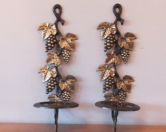May include: A pair of black metal wall candle holders with gold grapevine and grape clusters. Each holder has a round plate for a candle.
