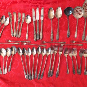 May include: A large collection of silver-toned metal flatware including various spoons, forks, and knives. The set features ornate handles with detailed patterns, including serving pieces like a ladle, a slotted spoon, and a cake server.