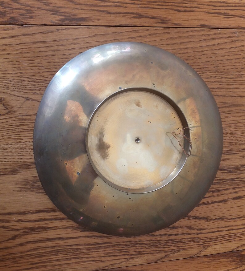 May include: A round, brass-coloured plate with a slightly raised centre. The plate has a smooth, shiny surface and a slightly worn appearance.