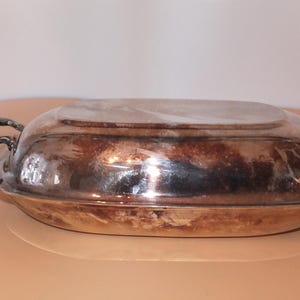 May include: A silver oval serving dish with a lid and two handles on each side. The dish is made of metal and has a shiny finish.