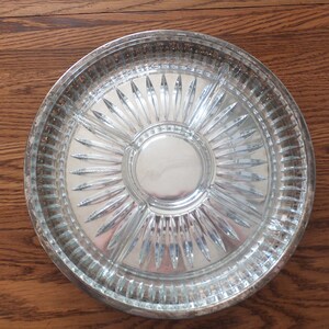 May include: A clear glass serving dish with a silver rim. The dish has a central section and four smaller sections around the edge. The dish has a starburst pattern.