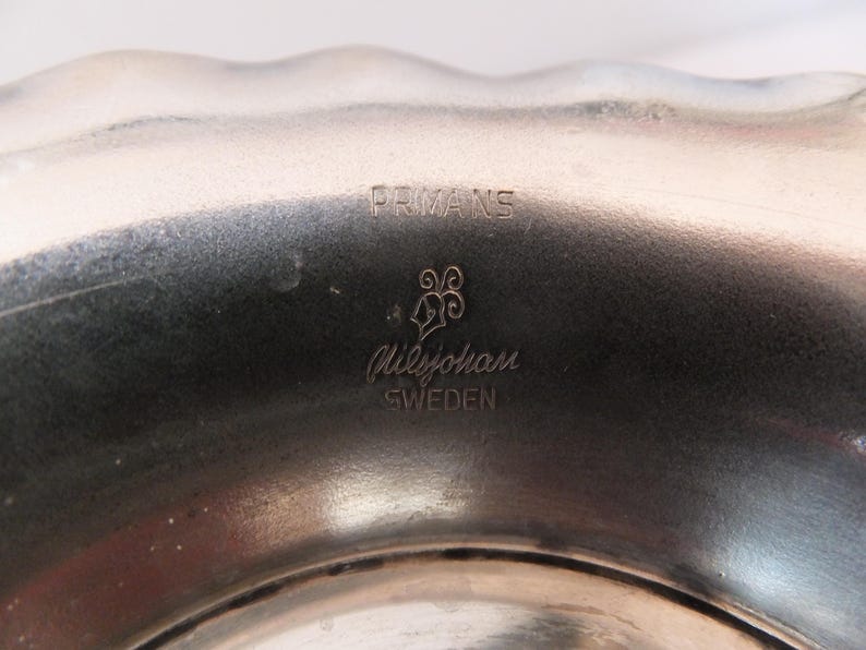 K&ouml;nnte beinhalten: Nahaufnahme einer silbernen Metallschale mit dem Text "PRMANS" und "GilleJohan SWEDEN", der auf den Boden graviert ist.