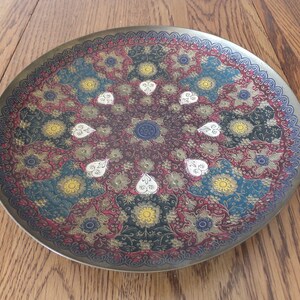 May include: A round brass tray with an intricate design featuring a floral pattern in shades of red, blue, yellow, and white.