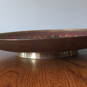 May include: A brown oval-shaped serving dish with a decorative pattern in shades of red, blue, and green. The dish has a silver-coloured base.